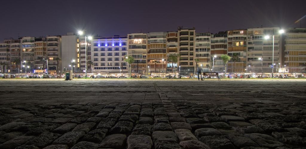 At night, there are buildings, one bench, and a road made by stone. 