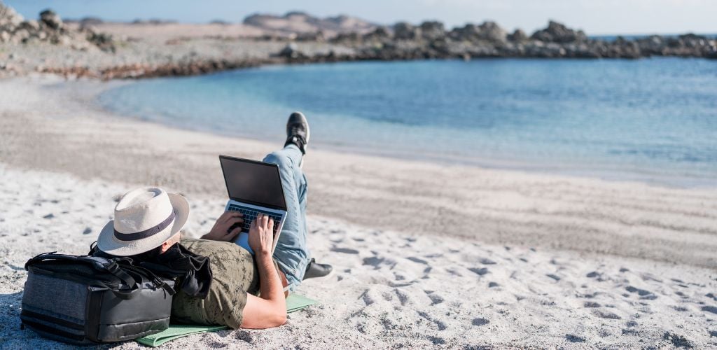 digital nomad lying on the beach outdoors alone working.