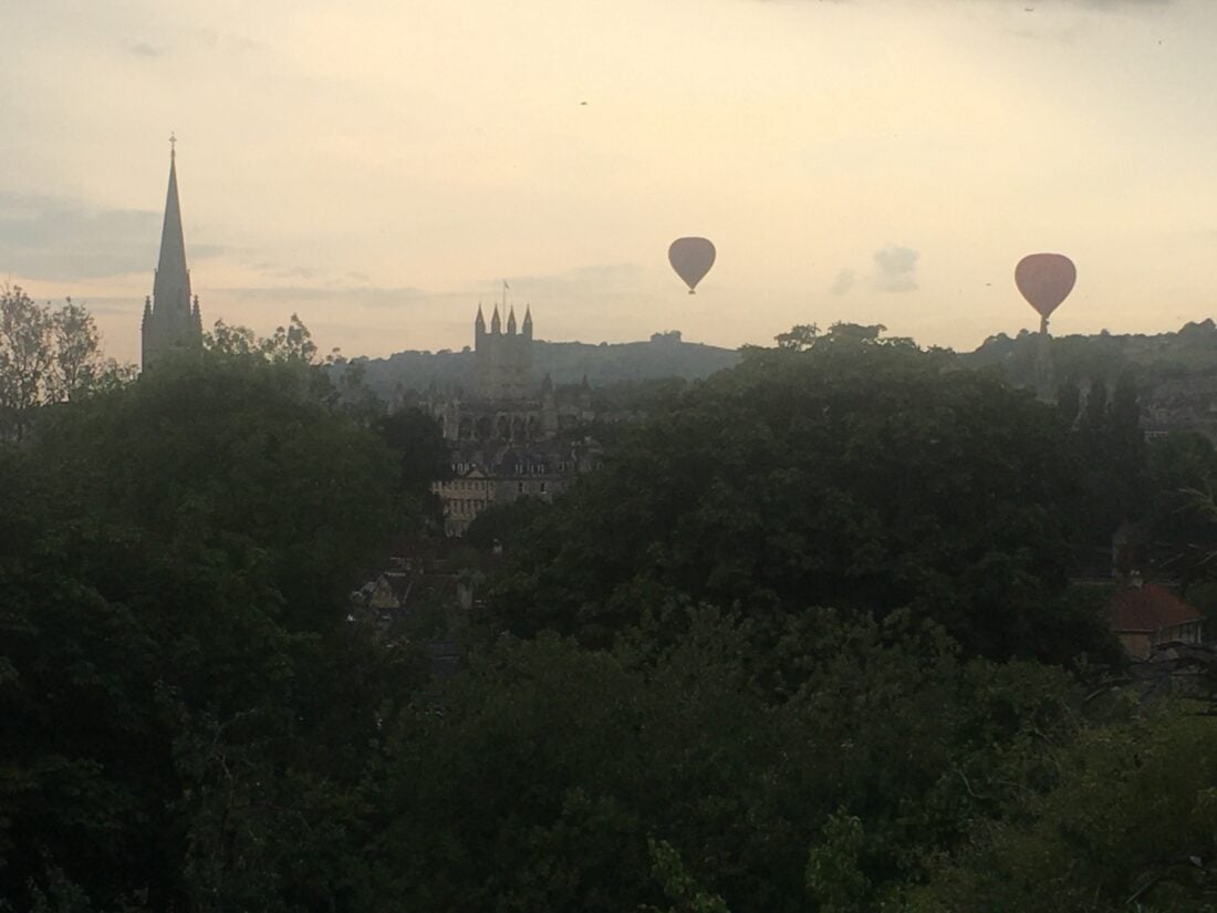 A historic structure and air balloon at the sky and surrounded by green trees. 