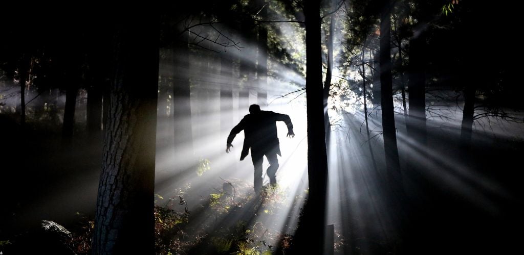 A scary shallow man running in the middle of the dark forest. 