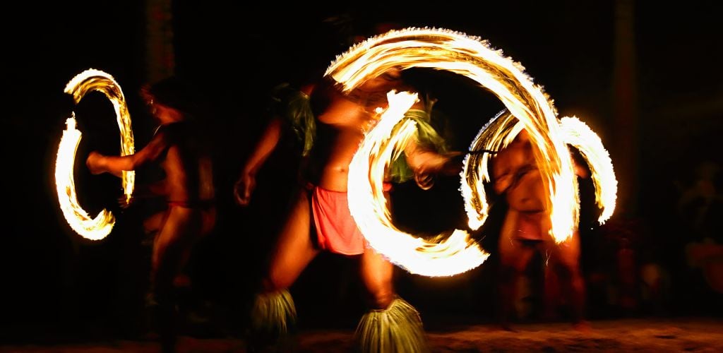 Three fire dancers at the Hawaii luau show, Polynesian hula dance men jugging with fire torches. 