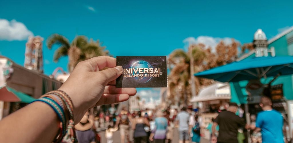 A Person Holding a Universal Studios Ticket, with a crowd of people inside the Universal Studios in the the background.