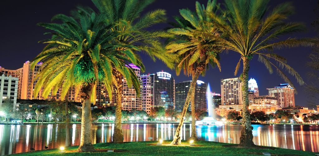 Orlando's downtown skyline panorama over Lake Eola at night with urban skyscrapers tropic palm trees and clear sky. 