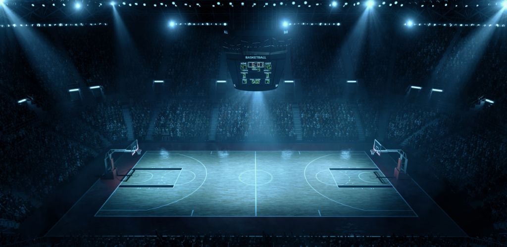 Indoor floodlit basketball arena is full of spectators. 