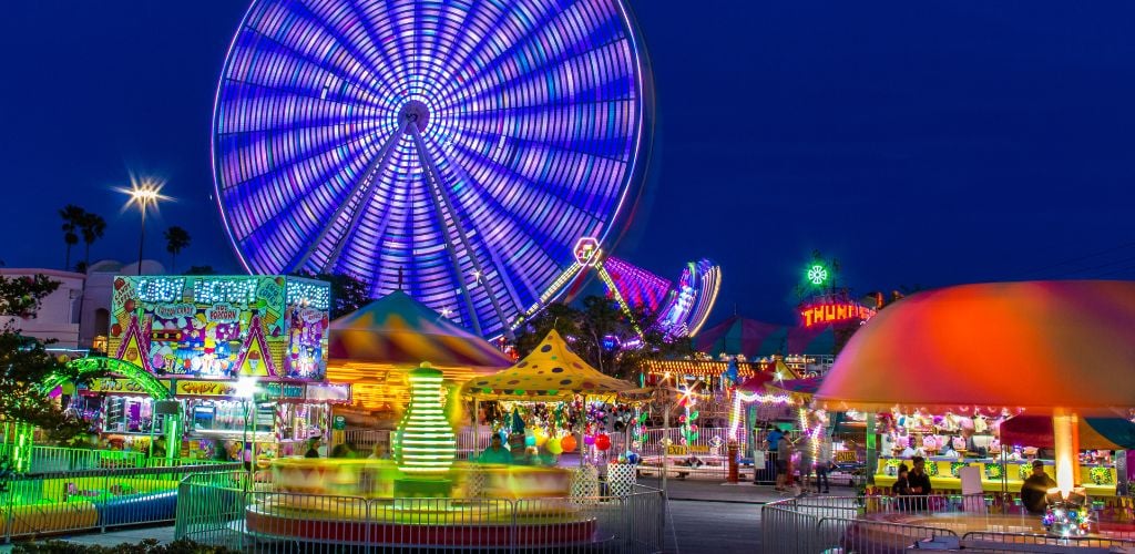 At Night, an Amusement Park. There includes a large Ferris wheel as well as other rides. 