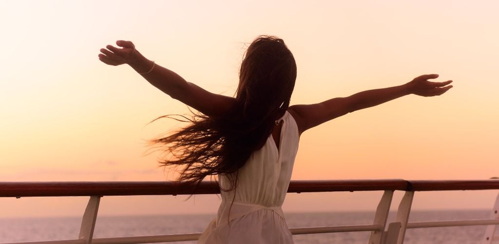 A woman wearing white dress in a cruise at sunset. 