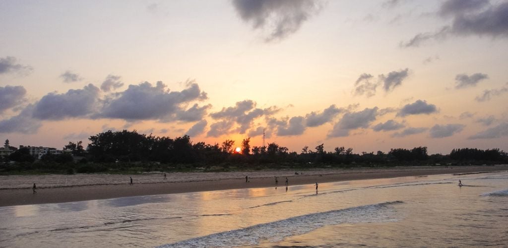 Sunset on the beach with a wavy sea and people enjoying the beach. 