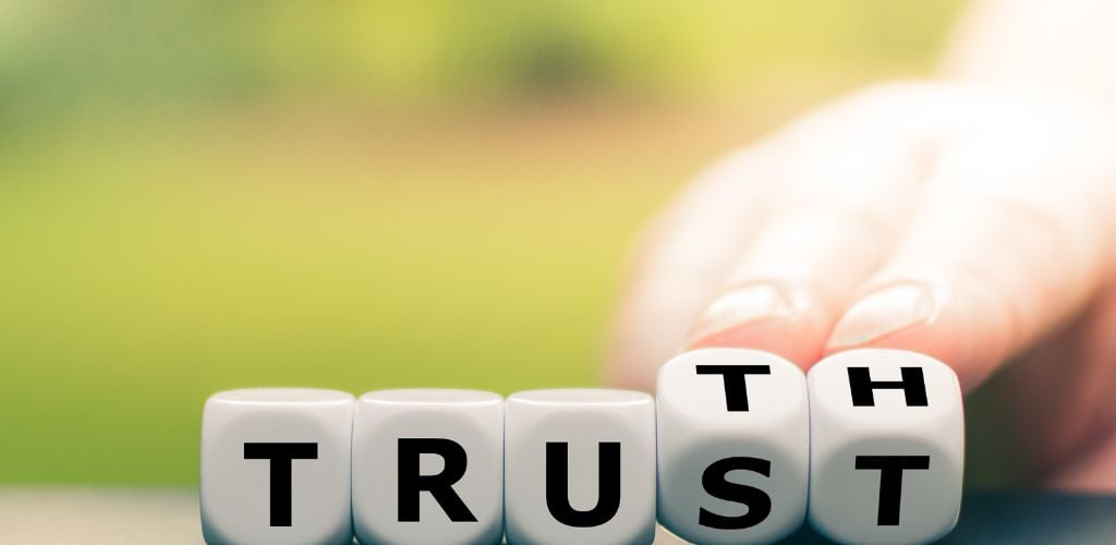 Truth instead of trust. Hand turns dice and changes the word "Trust" to "Truth".