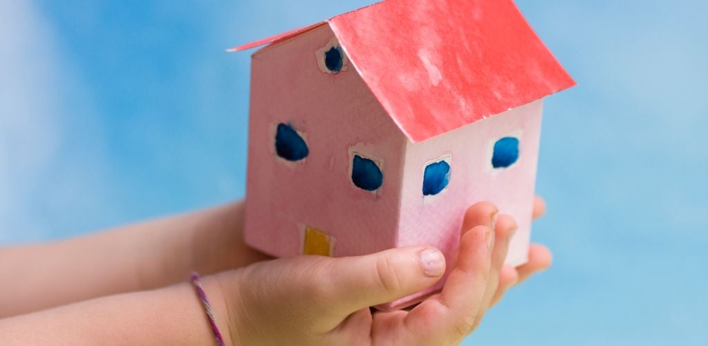 Painted carboard house in a child's hands. Useful to construction concepts. 