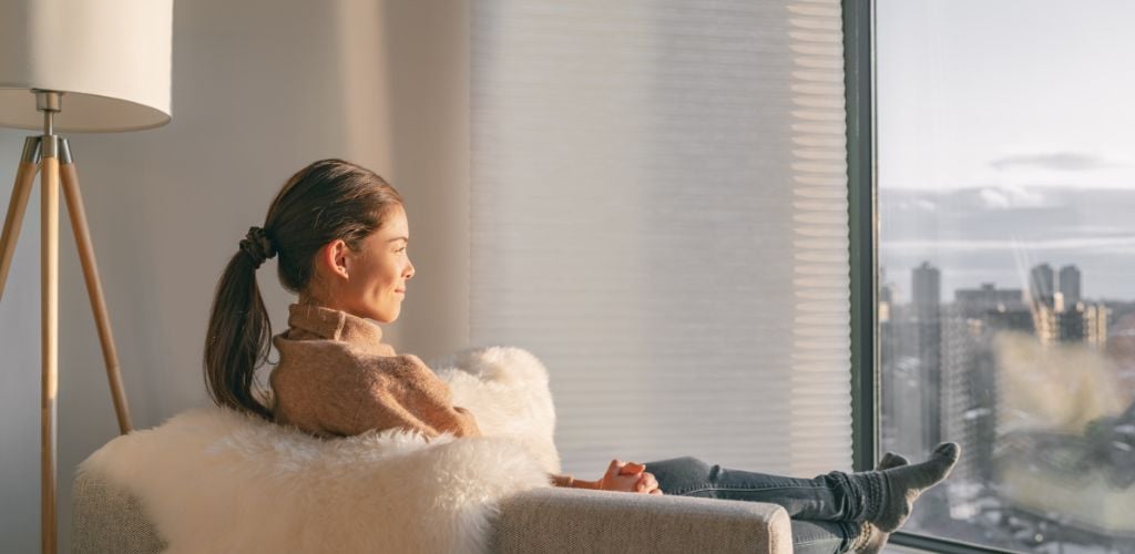Woman relaxing pensive looking out the window sitting on living room sofa enjoying free time. 