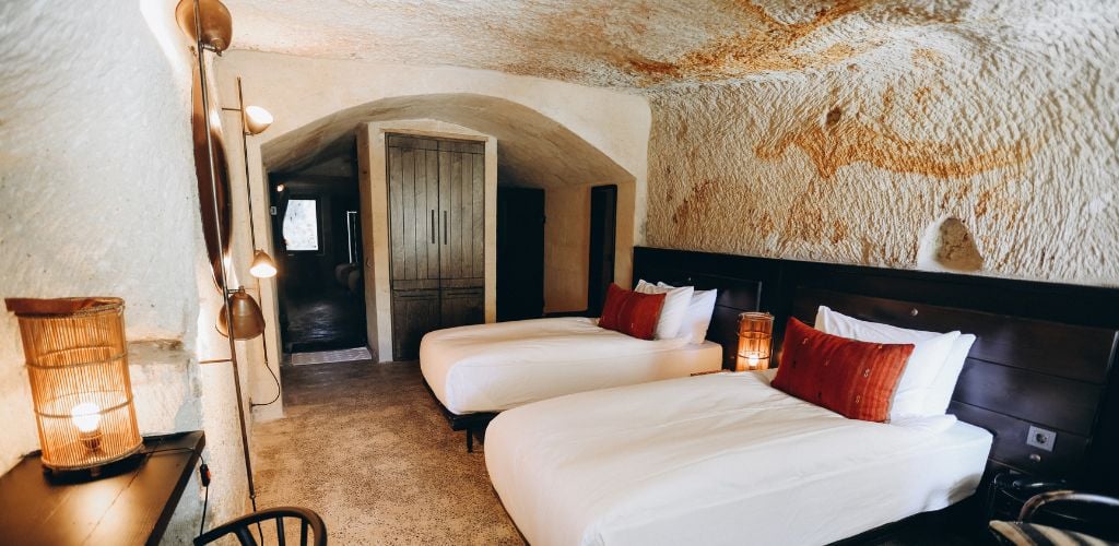 A two single bed in a cave hotel with lamps and cabinets. 