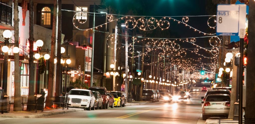 A street in Ybor City, street lights and cars parked on the side street, and running cars and buildings on the side street. 