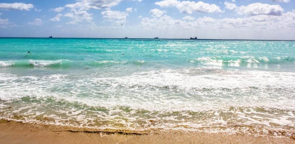 A white beach sand, clear water, and a boat in the distance. 