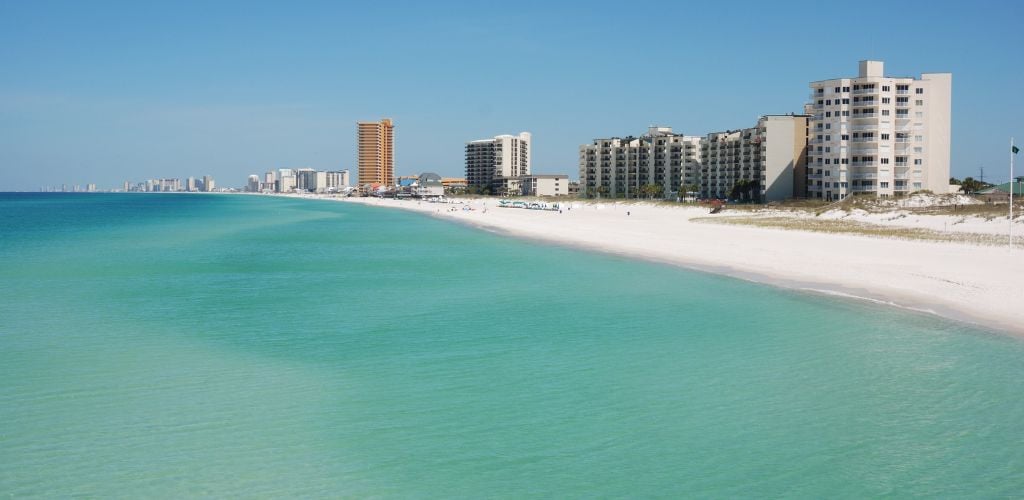 A building structure near the shore, white sand, and clear sea water. 