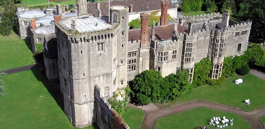 The historical castle of Thornbury. has a big garden on the front. and has a white table and chair.