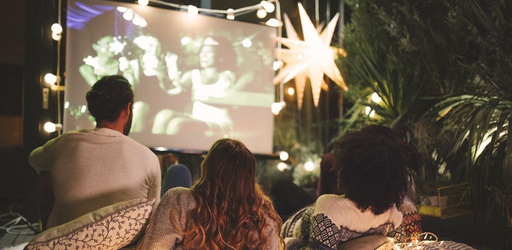 A man and two women are watching a movie outdoor. 