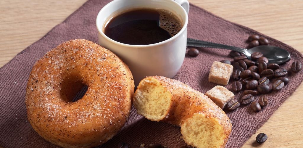 A cup of hot coffee with a classic donut for breakfast is on the table. 