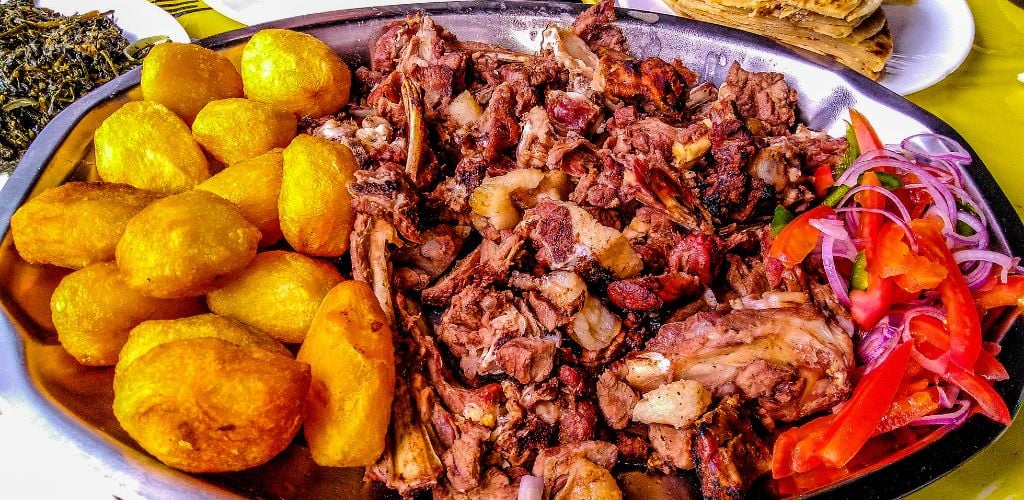 Sharing platter of a traditional Kenyan dish, Nyama Choma, and accompaniments of kachumbari salad, sukuma wiki, chapati, and roast potatoes.