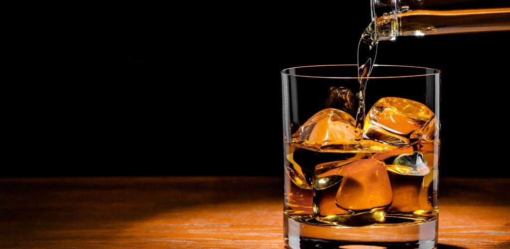 Pouring whiskey drink into glass on a wooden table with a black background. 