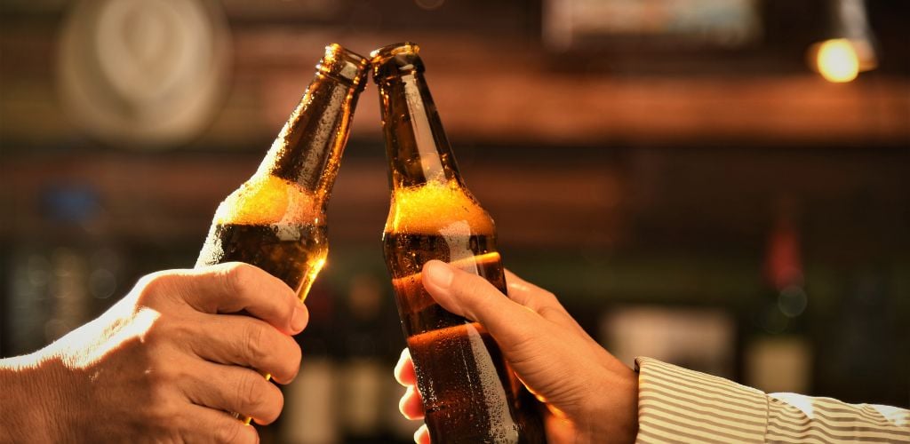 Two hands of men toasting a beer bottle...