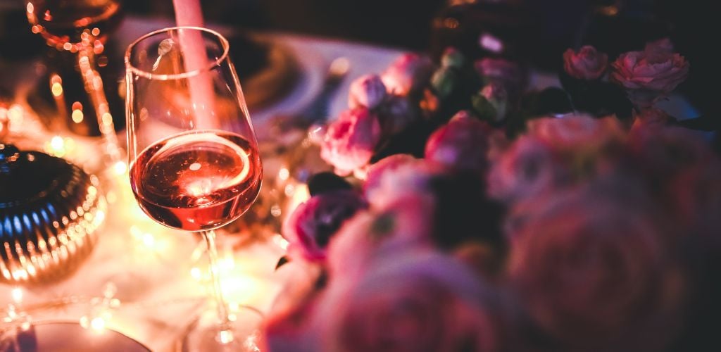 Glass of Rose Wine at a elegant table with pink roses on the side.
