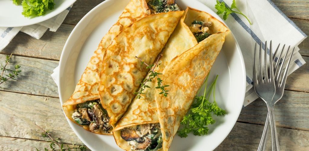Savory Homemade Mushroom and Spinach Crepes. two forks and a napkin on the side. 