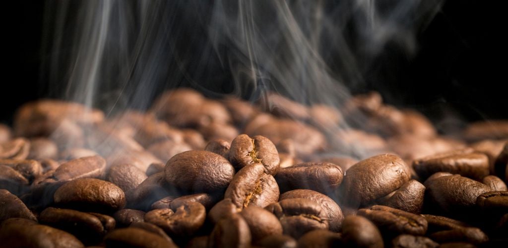 Roasting coffee beans with smoke wafting up on a black background. 