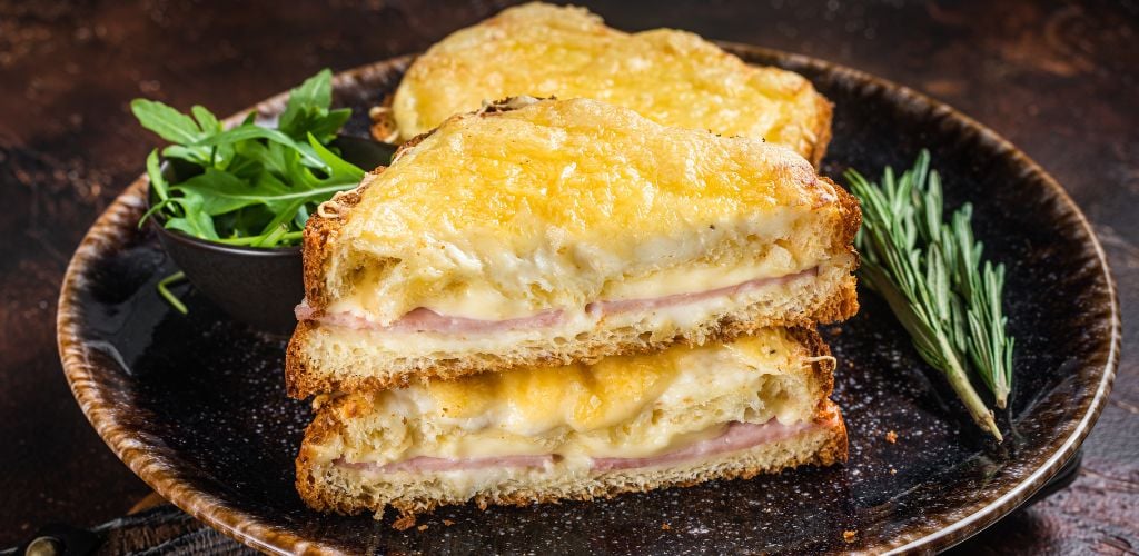 Croque Monsieur toasted sandwich with cheese, ham, gruyere, and Bechamel sauce. Dark background top view. 