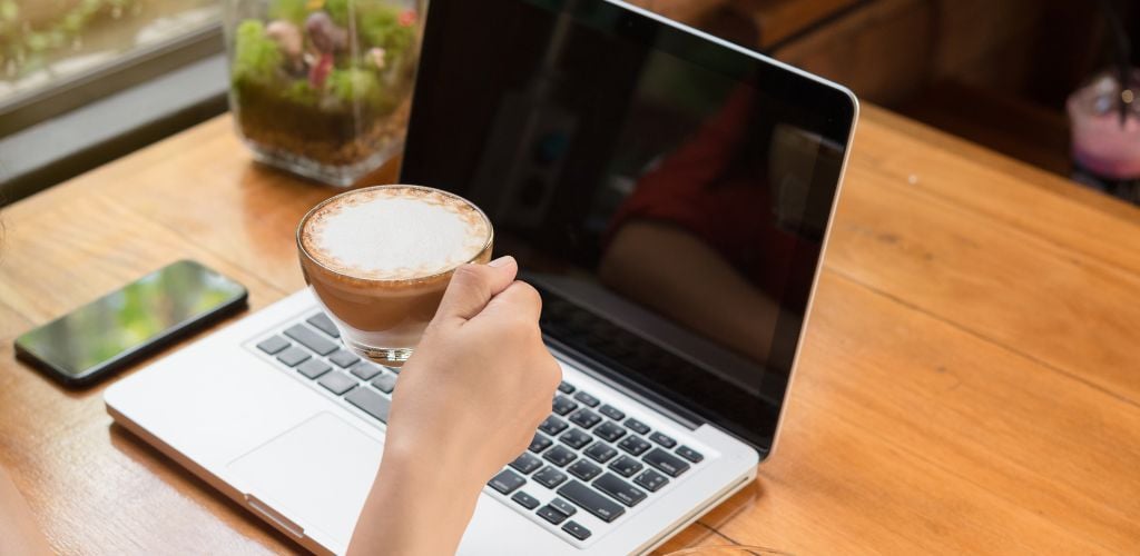 Young woman using laptop and drinking coffee in coffee shop
