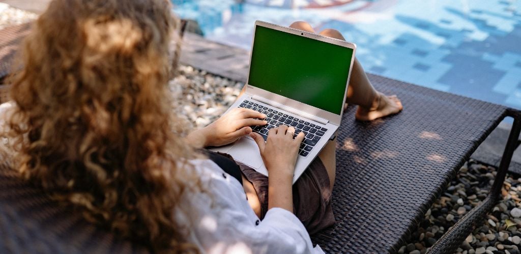 Unrecognizable female remote employee working on laptop near swimming pool