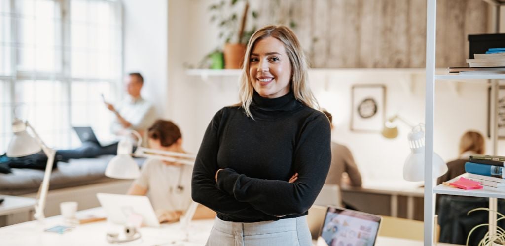 A woman standing and a busy people working on her background. 