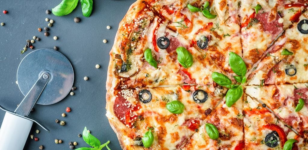 Italian pizza, basil and pizza knife on a dark background. top view. 