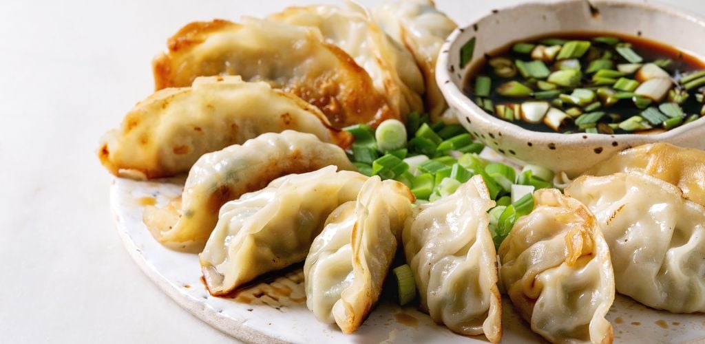 Fried asian dumplings Gyozas potstickers in white ceramic plate served with bowl of soy onion sauce over white marble table. Clove up. Asian dinner. 