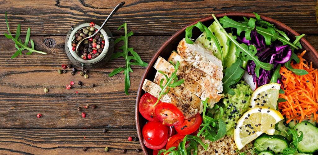 Healthy food. Buddha bowls lunch with grilled chicken and quinoa, tomato, guacamole, carrot, red cabbage, cucumber, and arugula on a wooden background—flat lay. Top view. 