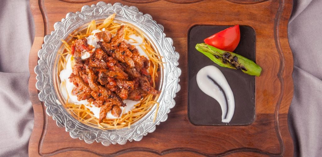 Marinated strips of veal with served with fried potatoes, garlic yoghurt, tomato sauce and served with fried tomatoes and green peppers.