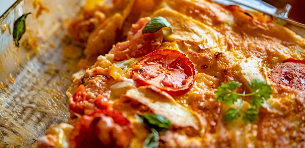 In a casserole dish, serve vegetable lasagna with a tomato and green leaf garnish on top. 