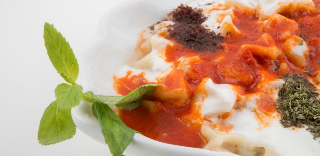 Dumpling topped with white and red sauce. a herb with a green leaf on top 