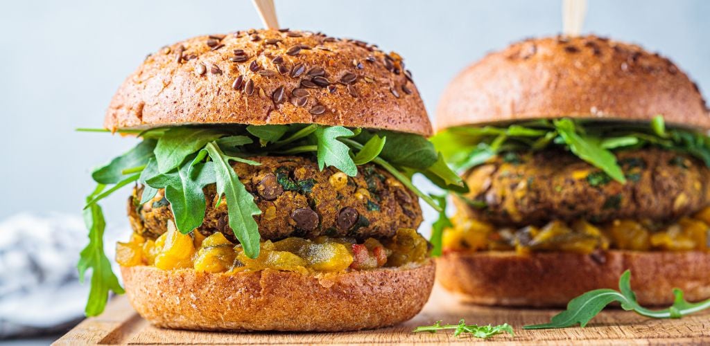 Two Vegan Lentil burgers with arugula mustard sauce and fresh vegetables on a wooden board.