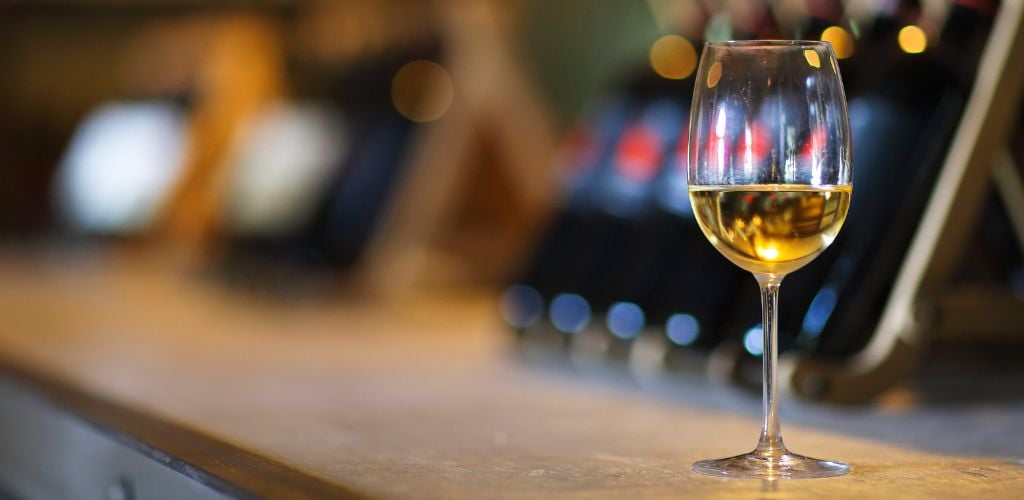 Wine bottles on a wooden shelf. Wine bar. Close up on a glass of white wine. 