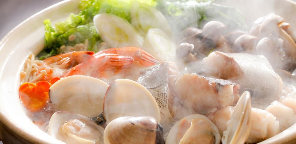 A steaming pot filled with fish, clams, shrimp, and veggies.