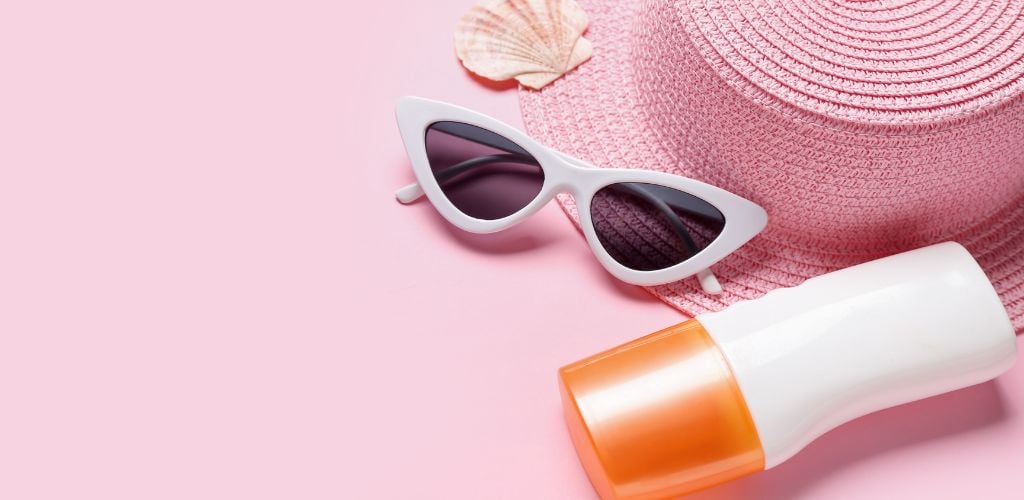 Bottle of Sunscreen Cream, Hat, Sunglasses, and Seashell on Pink Background. 