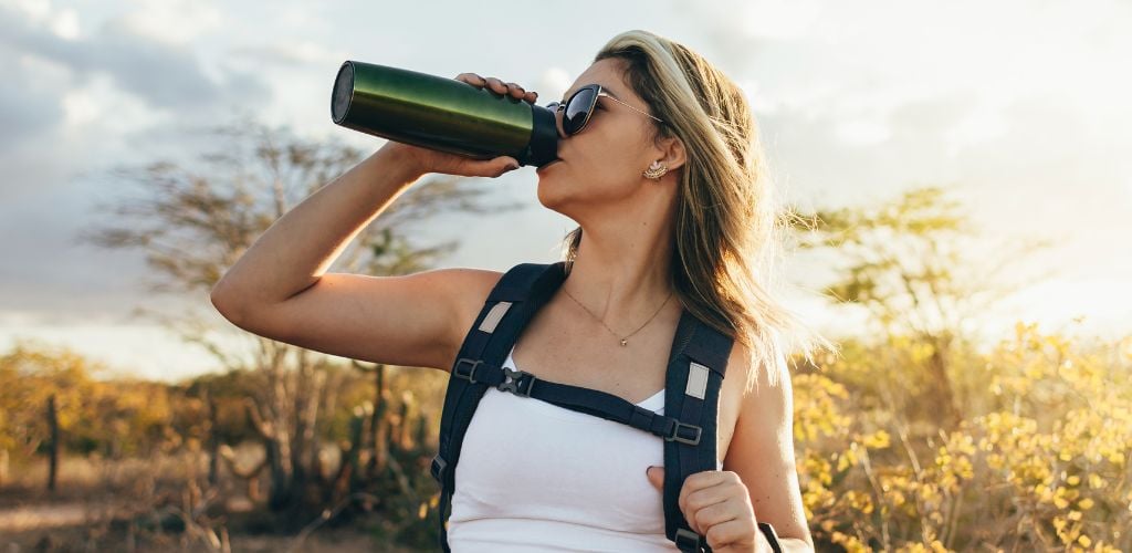 Woman taking a break to drink from a water bottle while hiking.