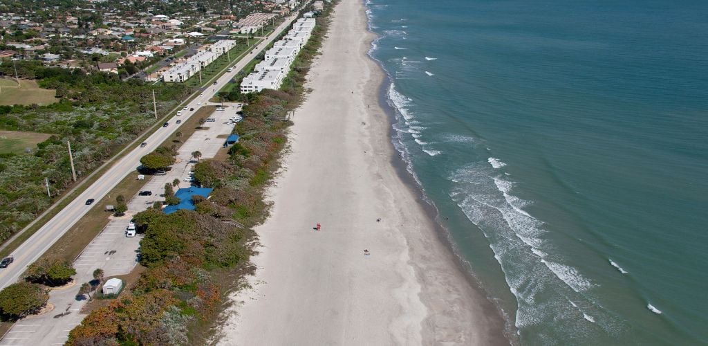 An aerial view of the beach, with a road on the right side and a parking area where the beach can be seen from overhead. 