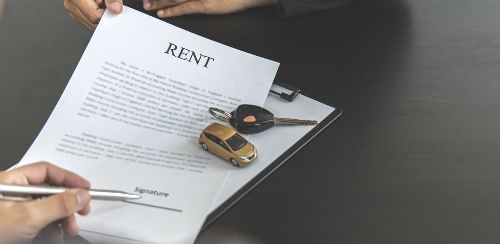 Person Signing Contract for Rent with car key and small car toy on the top. 