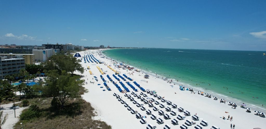 A white sand beach with a tent near the shore, buildings on the side, and trees. 