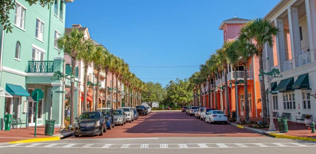 A street with colorful buildings on both sides, coconut trees, and cars parked on the side street. 