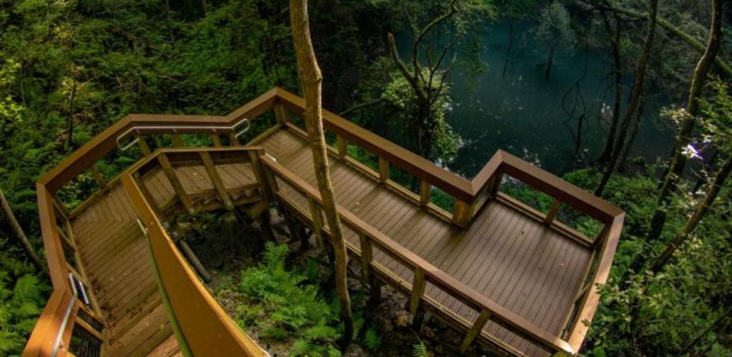 A stairwell and a little balcony with views of a lake surrounded by green trees. 