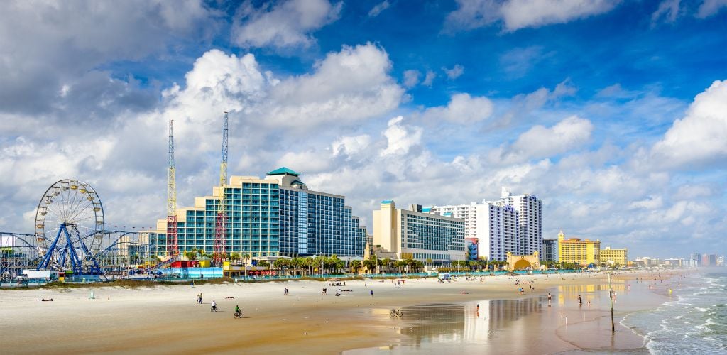 A structure and an amusement park, people enjoying themselves on the beach, and a cloudy sky. 