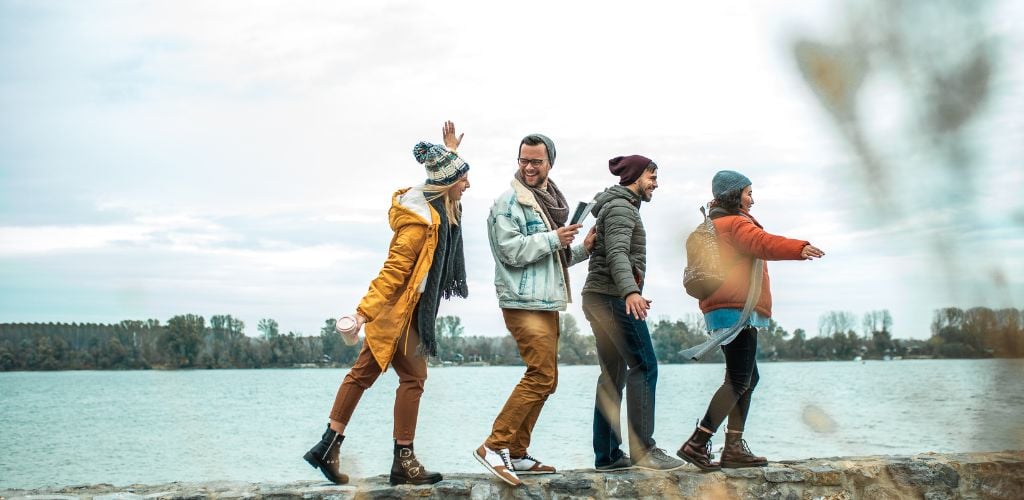 A group of four friends is by the river walking on the stone edge and exploring the beauty of nature. 