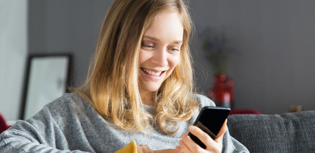 A cheerful woman using smartphone in living room. 